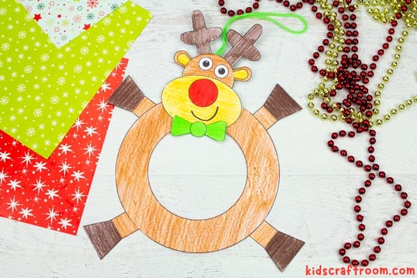 A completed Reindeer Wreath lying on a white background surrounded by wrapping paper and Christmas decorations.
