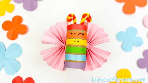 A Rainbow Butterfly Craft on a white background with colourful paper flowers scattered around it.