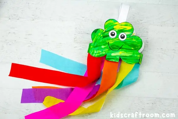 A close up of a green Scrape Painting Shamrock Windsock Craft with rainbow streamers.