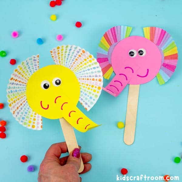 2 Cupcake Liner Elephant Puppet Crafts on a blue background. One is yellow and one is pink.