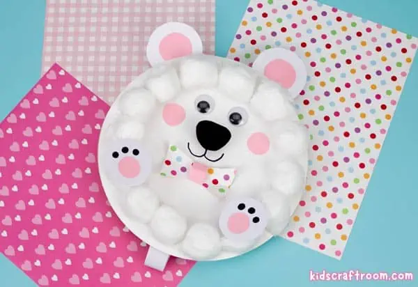 A paper plate rocking polar bear lying on pink patterned paper.